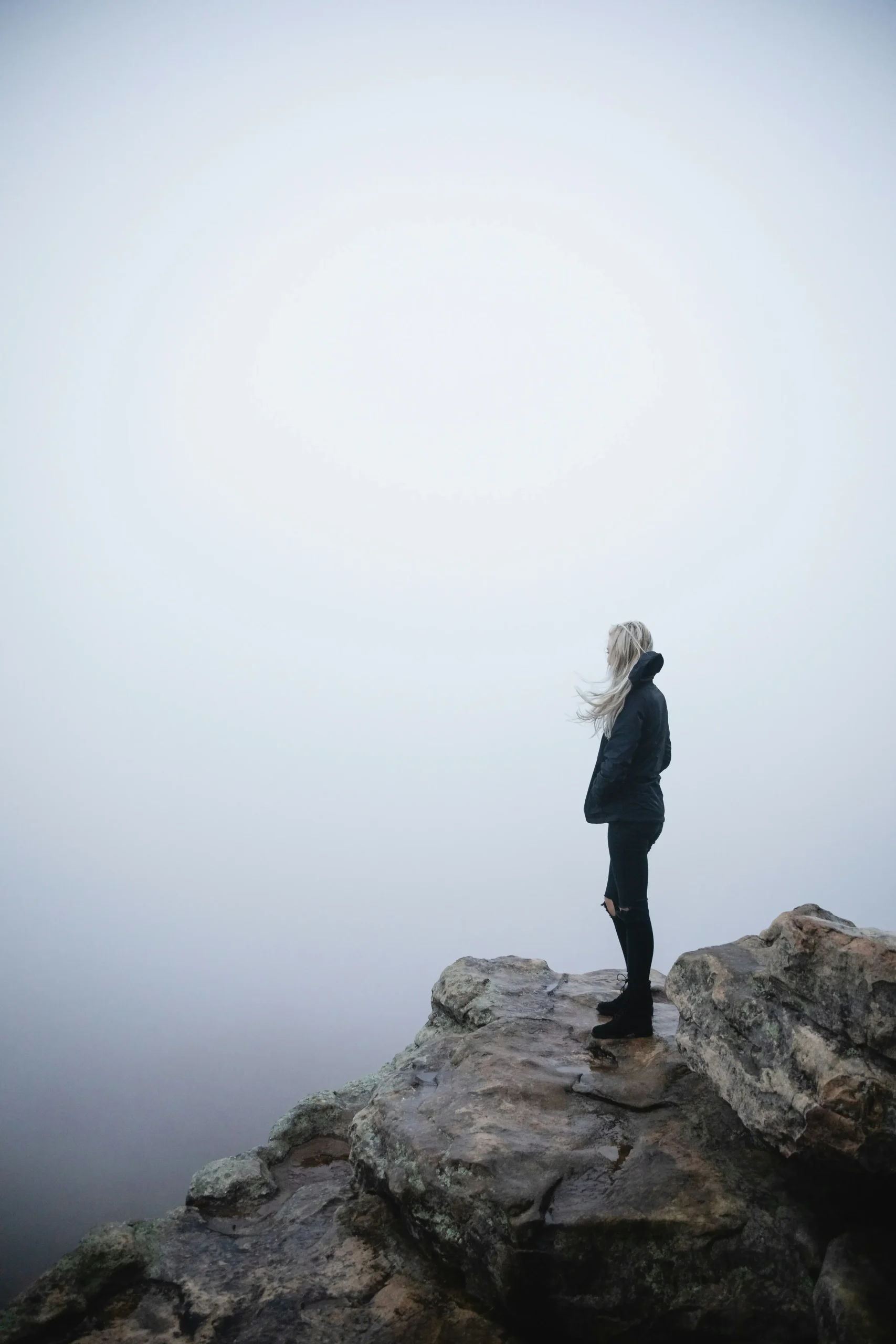Mujer de pie sobre unas rocas mirando la niebla